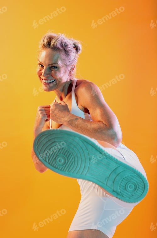 Preview: Smiling senior athlete kicking and exercising on orange background