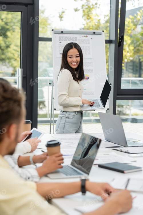 Preview: happy asian woman holding laptop with blank screen near flip chart with graphs during business