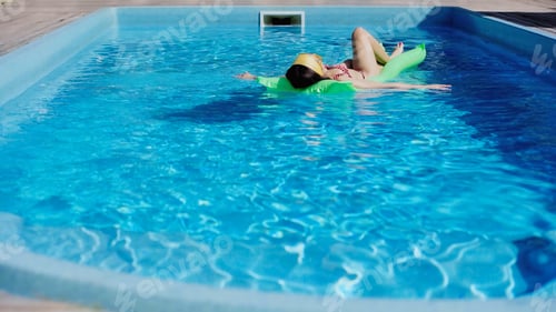 Preview: young woman swimming on pool float in blue water
