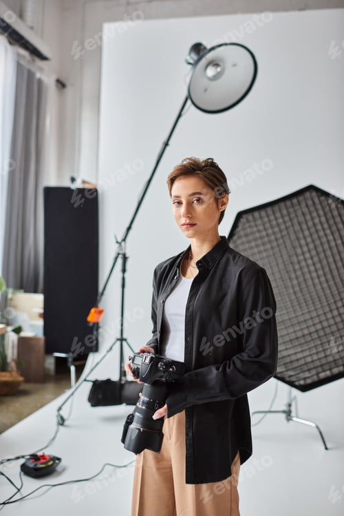Preview: attractive short haired female photographer in casual attire looking at camera while at her studio