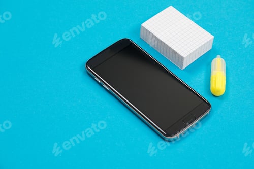Preview: Black smartphone, a pile of scratch paper and one yellow textliner on blue background isolated