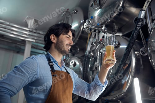 Preview: A man is holding a glass of beer while inside a brewery setting