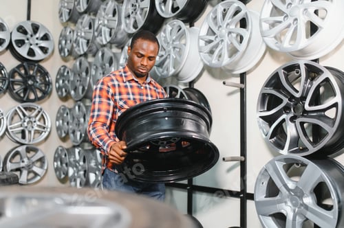 Preview: African american Car mechanic holding car rims ready to mount the wheels in workshop