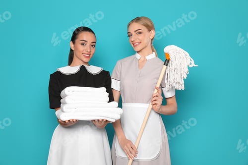 Preview: Young chambermaids with stack of clean towels and mop on color background