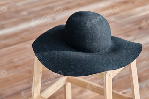 Preview: black women's hat with wide brim on a wooden chair.