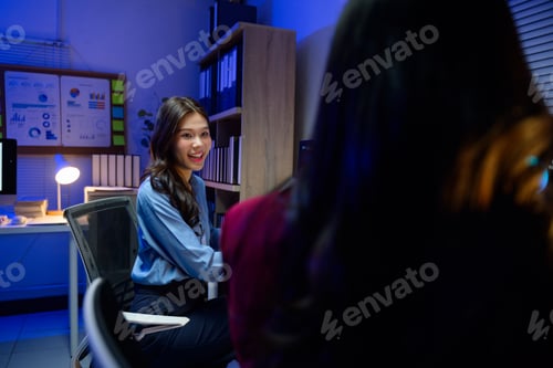 Preview: Asian businesswomen working late in office at night discussing project together