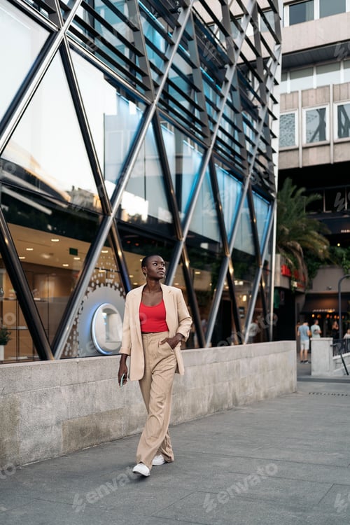 Preview: Stylish young woman walking on the city looking away while holding her phone