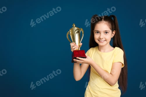 Preview: Happy girl with golden winning cup on dark blue background. Space for text