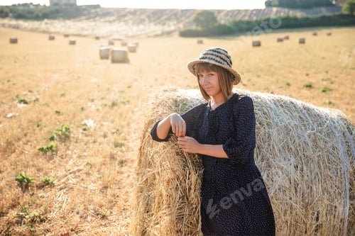 Preview: beautiful young woman leaning at hay bale and looking at camera, provence, france