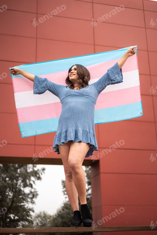 Preview: Trans woman standing with trans flag. She is proud and happy.