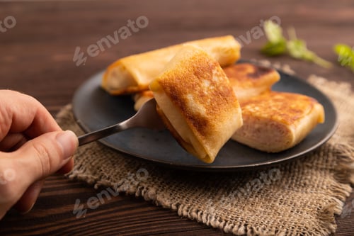 Preview: Fried crispy pancakes with meat and cheese with hand on brown wooden and linen textile. side view