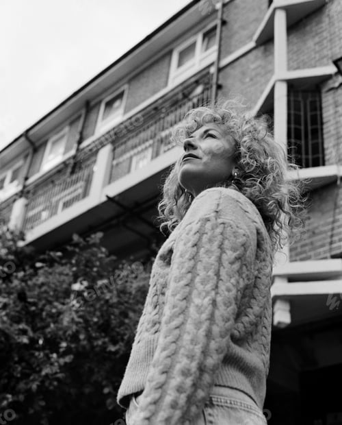 Preview: Low point of view of curly woman looking away in front of building.