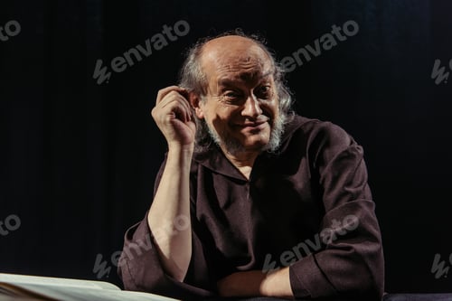 Preview: smiling monk looking at camera while sitting near bible isolated on black