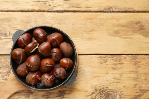 Preview: Fresh edible sweet chestnuts in frying pan on wooden table, top view. Space for text