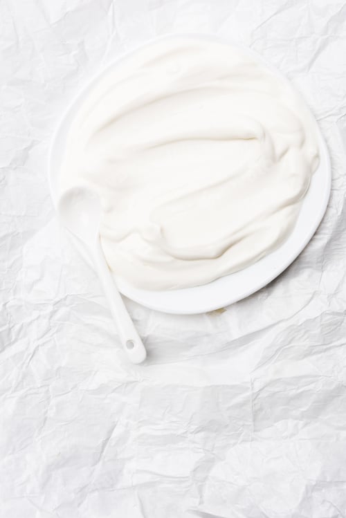 Preview: top view of sour cream on plate with spoon on white crumpled paper