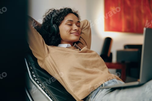 Preview: Smiling woman in headphones is listening music during break on work on laptop at home