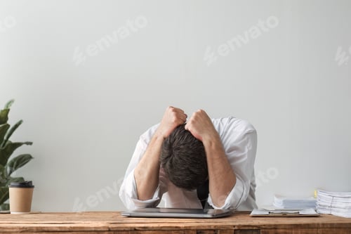 Preview: Unhappy young businessman feeling bored and stressed at work looking at laptop with hopeless