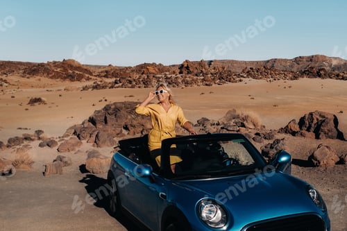 Preview: Girl in yellow dress enjoying a road trip in a convertible through a deserted valley with mountains