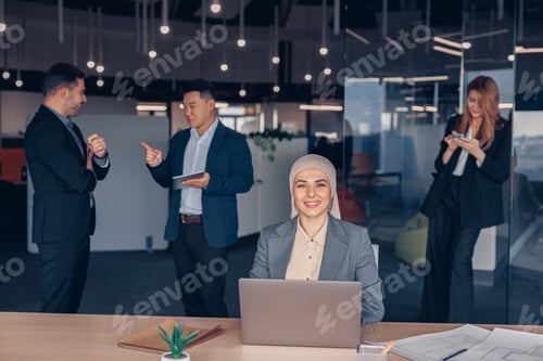 Preview: Smiling muslim businesswoman in hijab working on computer while sitting in modern office