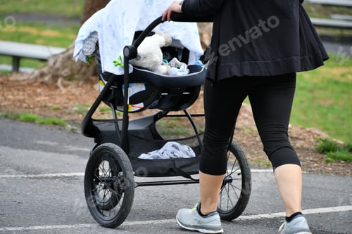 Preview: Woman Pushing Stroller Outdoors on Gray Asphalt