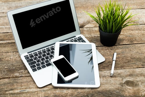 Preview: Workspace setup featuring a laptop, tablet, smartphone, and plants on a wooden table during daytime