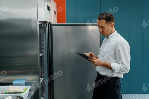 Preview: Professional chef using tablet computer for recipes while working in modern kitchen cooking concept
