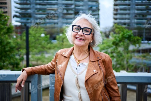 Preview: Portrait of attractive Caucasian mature woman posing leaning on rail in front of garden city area