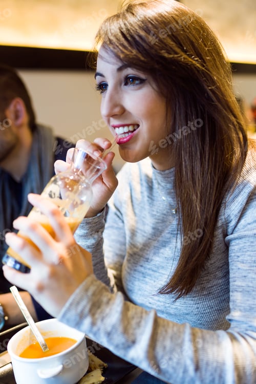 Preview: Beautiful young woman drinking orange juice in restaurant.