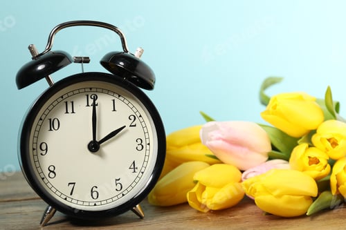 Preview: Spring time. Alarm clock and beautiful tulips on wooden table against light blue background