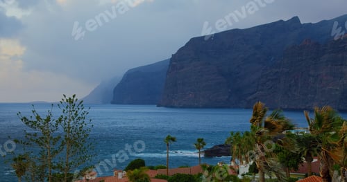 Preview: Tenerife at sunset, blue hour. Mountain resort town with hotels, palm trees. Los Gigantes Cliffs