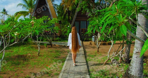 Preview: Beautiful rear view of girl with red long hair walks in tropical indonesian park in Bali Island