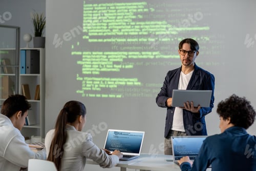 Preview: Serious teacher with laptop standing by board with information