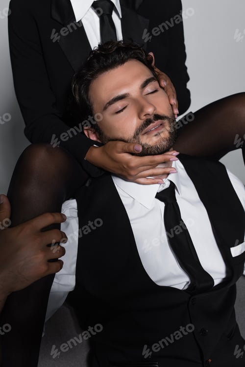Preview: passionate woman in black tights seducing elegant man sitting with closed eyes on grey background