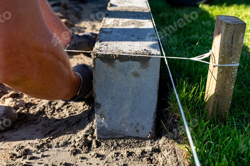 Preview: A man lays concrete blocks on a poured foundation, gluing them with mortar.