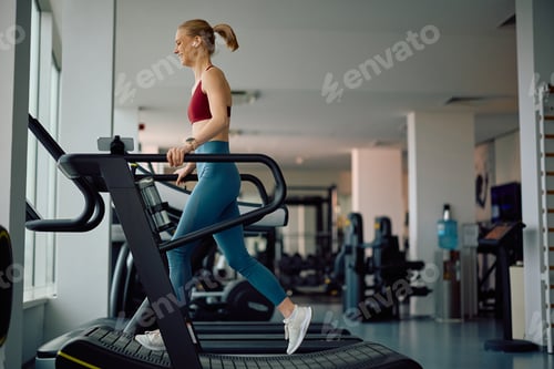 Preview: Happy sportswoman running on curved treadmill during sports training in health club.