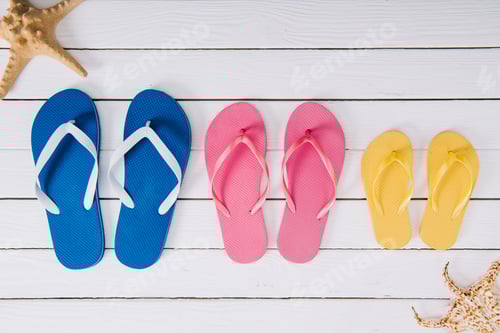 Preview: top view of yellow, blue and pink flip flops on white wooden background