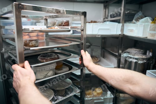 Preview: Cropped chef holding dishes on shelves in refrigerator storage in restaurant