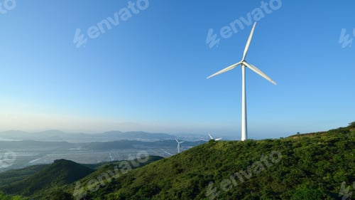 Preview: White wind turbines atop a mountain peak with a bright blue sky in the background