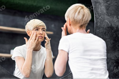 Preview: Mature Woman Looking At Wrinkles Under Eyes Standing In Bathroom