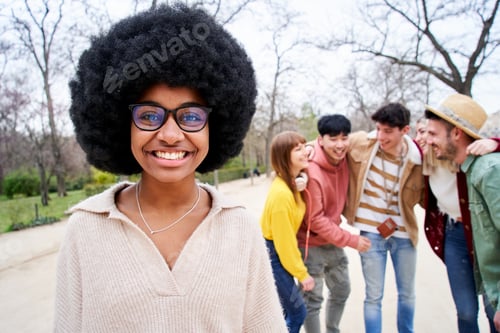 Visualização: Jovem garota afro sorridente olhando para a câmera ao ar livre com grupo de amigos