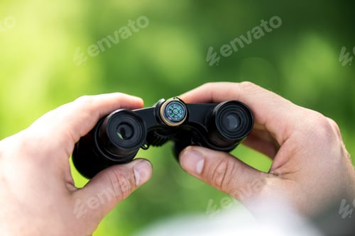 Preview: cropped shot of man holding binoculars on blurred green background