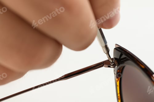 Preview: Handyman repairing sunglasses with screwdriver on white background, closeup