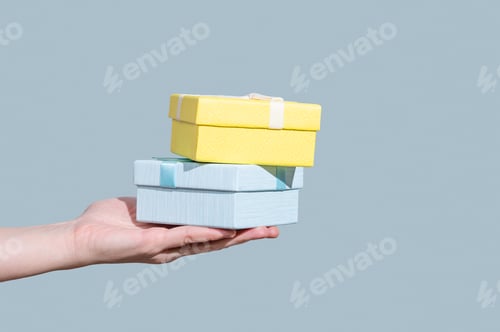 Preview: Two blue and yellow gift boxes in hand on light background.