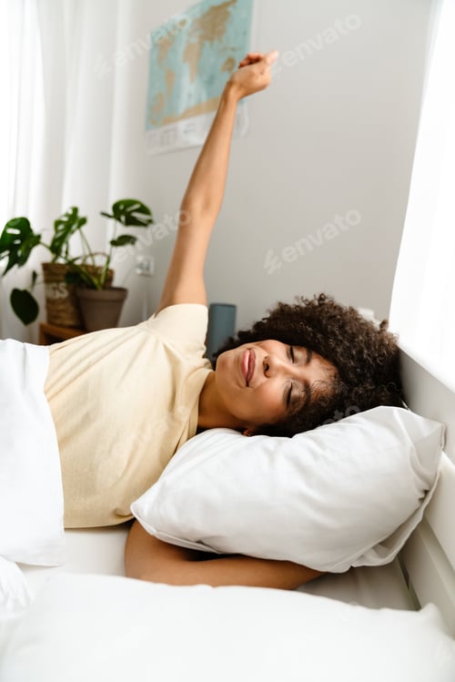 Preview: African american young woman stretching in bed after sleep at home