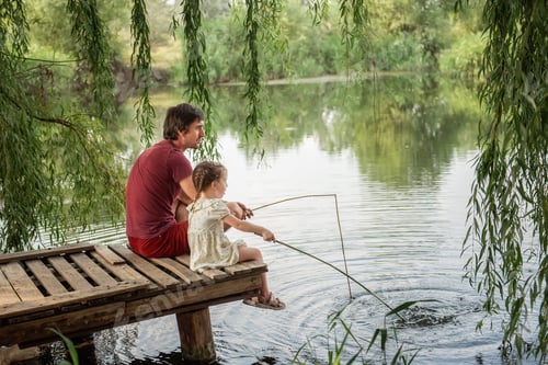 Preview: Father and daughter are sitting on wooden pier by the lake, playing fishing. Countryside vacation