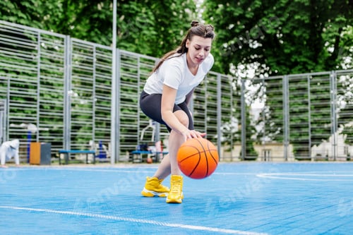 Preview: Young athletic woman is training to play basketball on modern outdoor basketball court. Happy woman