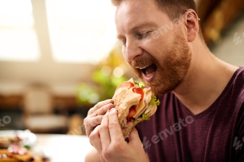 Preview: Man with eyes closed enjoying in a sandwich for breakfast at home.