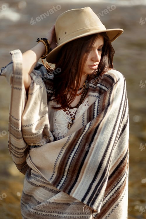 Preview: beautiful woman traveler wearing hat and poncho standing in water of river