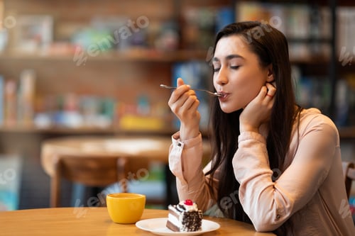 Preview: Happy arab lady enjoying dessert and coffee with closed eyes, sitting in cafe, having break at work