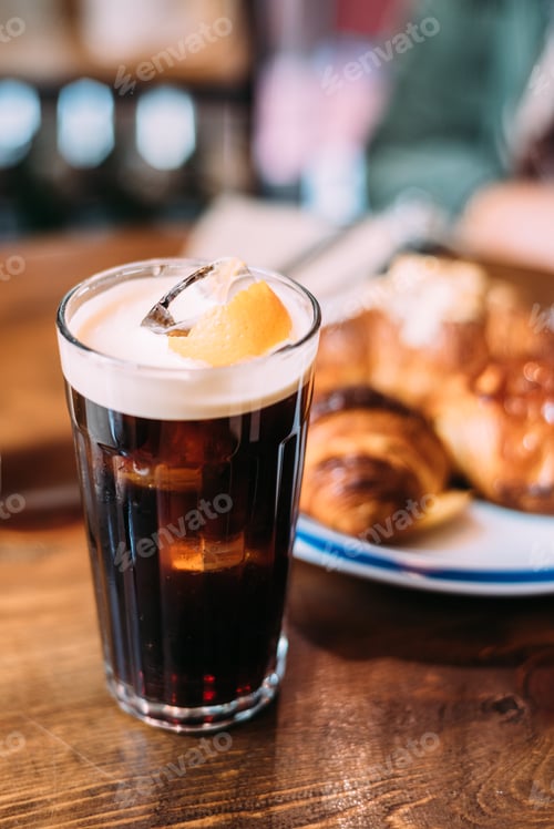 Preview: Ice coffee in a tall glass with cream poured over on a old rustic wooden